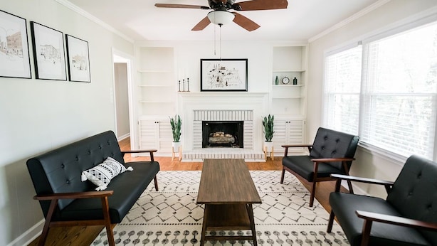 A living room with a fireplace, a ceiling fan, and a patterned rug. - Spacious 6 bedroom home near Downtown Macon! (Macon)
