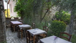Un área de comedor al aire libre con suelo de piedra, mesas y sillas de madera y un muro de piedra de fondo.