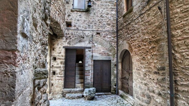 Un estrecho callejón empedrado con paredes de piedra, una puerta de madera y un pequeño banco de piedra.