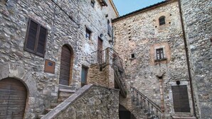 Un estrecho callejón de piedra con una escalera que lleva a un edificio con contraventanas de madera y una barandilla de metal.