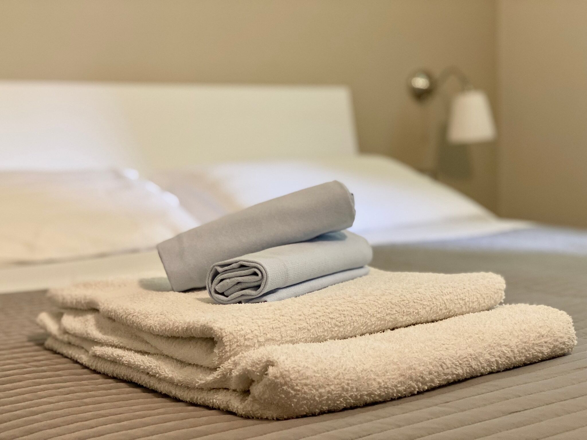 A neatly made bed with white and grey towels, a lamp on the side, and a textured bedspread.