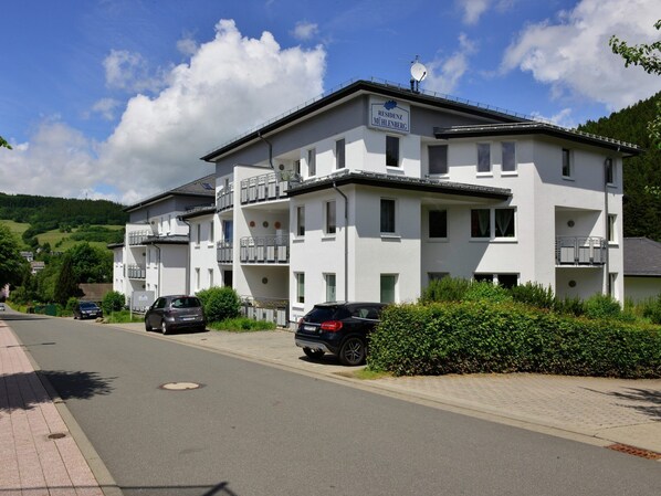 A multi-story white building with balconies, labeled "RESIDENZ MÜHLENBERG," parked cars, and a clear sky.