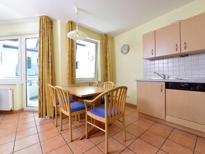 A dining area with a table and chairs, a kitchen with cabinets and a Bosch dishwasher, and a window with curtains.