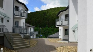 A building with a central courtyard, a staircase leading to an upper floor, and a view of a forested hill in the background. - Modernes Apartment in Willingen mit Balkon (Willingen)