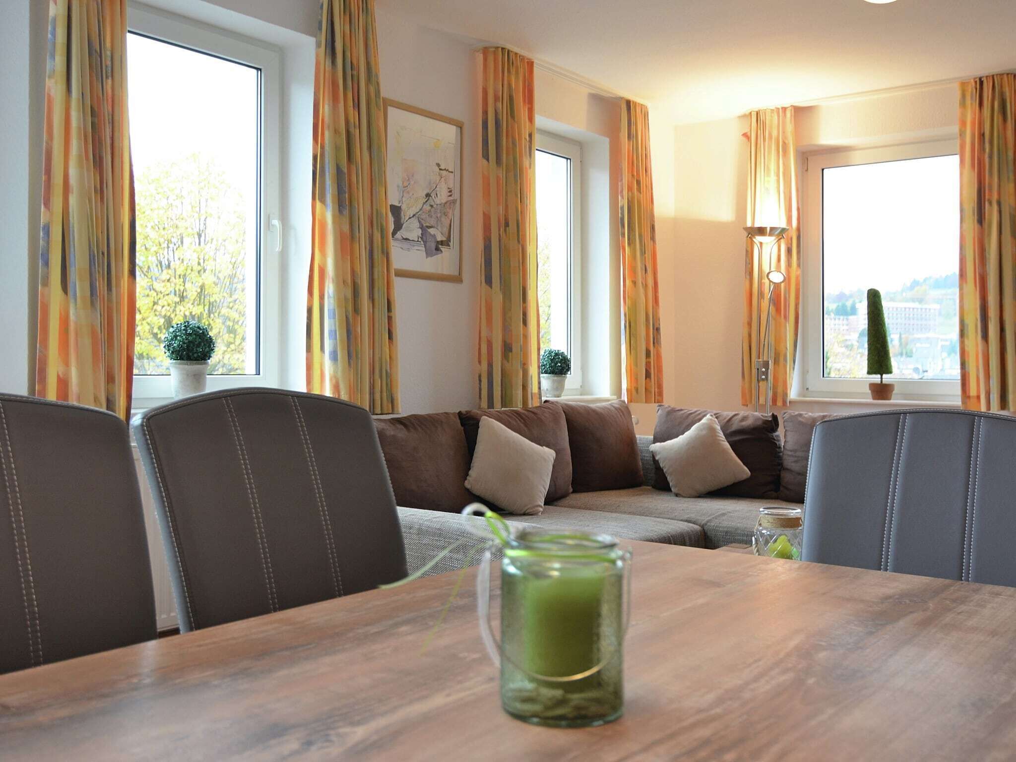 Ein gemütliches Wohnzimmer mit einer Couch, Sesseln, einem Tisch mit einem Glas und einer Lampe.