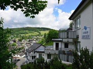 Un immeuble résidentiel, identifiable grâce à une enseigne indiquant qu’il s’agit d’une résidence pour personnes âgées, est entouré de verdure et offre une vue sur un village.