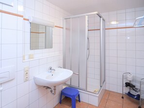 Kylpyhuone, jossa on valkoinen pesuallas, peili ja suihkukaappi.