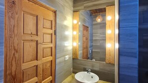 Une salle de bain avec des murs recouverts de panneaux de bois, une porte en bois, un meuble-lavabo avec un évier et un miroir avec éclairage.
