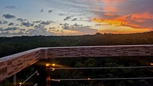 Une vue sur le coucher de soleil depuis un balcon doté d’une balustrade en pierre, donnant sur une zone boisée.