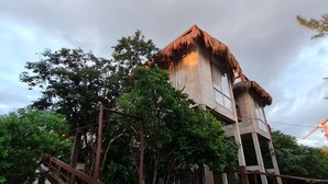 Un bâtiment traditionnel avec un toit de chaume, entouré d’une végétation luxuriante et d’une clôture en bois.
