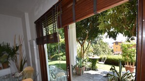 A patio with a glass door leading to a garden, a round table with a chair, and potted plants.