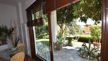 Eine Terrasse mit Glastür zu einem Garten, ein runder Tisch mit einem Stuhl und Kübelpflanzen.