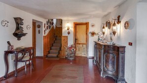 Ein Flur mit einer Holztreppe, einem Holztisch, einem Stuhl, einem Konsolentisch mit Dekoration und Wandleuchten.