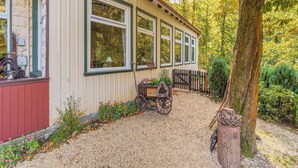 A rustic cabin with a gravel driveway, a wooden cart, and a wooden fence.
