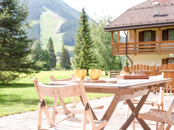 A wooden table with chess set and bowls, set outdoors with a mountain view.
