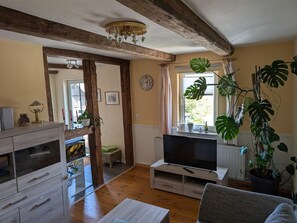 Un salon avec un plafond en bois, un téléviseur pos é sur un meuble, un canapé et une plante en pot.