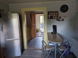 A compact kitchen with a refrigerator, a coffee maker, and a dining area with a table and chairs. - Ferienwohnung in den Hüttenroder Bergen (Hüttenrode)