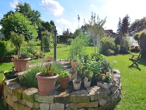 A garden with a stone circular planter filled with various potted plants. - Ferienwohnung in den Hüttenroder Bergen (Hüttenrode)