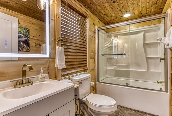 Un baño con detalles de madera, un lavamanos con grifo dorado, un inodoro y zona de ducha con mampara de vidrio.