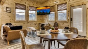 A cozy cabin interior with a wooden interior, a round dining table, and a television mounted on the wall. - In-Town Smoky Mountain Views • No Steep Roads • Fully fenced Area for Pets. (Sevierville)