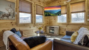 A cozy cabin interior with a leather sofa, a small table with a vase, and a fireplace. - In-Town Smoky Mountain Views • No Steep Roads • Fully fenced Area for Pets. (Sevierville)
