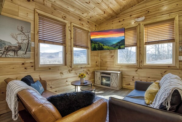 A cozy cabin interior with a leather sofa, a small table with a vase, and a fireplace.
