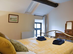 Quarto com cama, radiador, janela e cómoda de madeira.