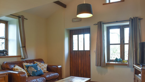 A living room with a brown leather sofa, a wooden coffee table, a wooden cabinet, and a large window with curtains.