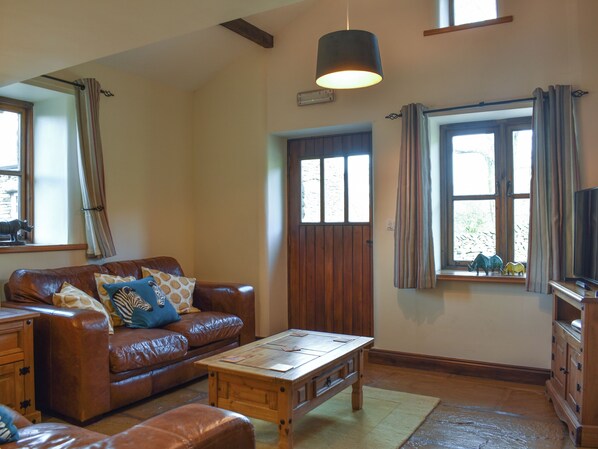 Un salon avec un canapé en cuir marron, une table basse en bois, un meuble en bois et une grande fenêtre avec des rideaux.