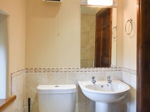 Un baño con inodoro y lavamanos, ambos blancos, con salpicadero de azulejos y marco de puerta de madera.