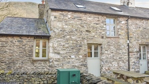 A stone building with a sloped roof, a chimney, and a green electrical box.