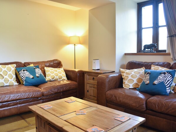 A living room with two brown leather sofas, each with zebra-patterned cushions, a wooden coffee table, a floor lamp, and a window with a decorative animal figure.