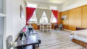Een kamer met een bed, een slaapbank, een eettafel met stoelen, een klein bureau en een raam met gordijnen.