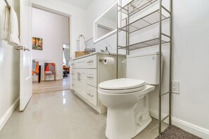 Un baño moderno con un inodoro blanco, un estante metálico y suelo de baldosas.