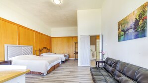 Een kamer met een houten vloer, twee bedden, een leren bank en een schilderij aan de muur.