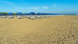 A beach with rows of sun loungers and blue umbrellas. - Apartment in Albarella near Beach & Activities (Albarella)
