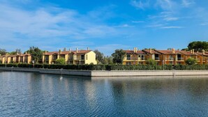 A waterfront hotel with multiple yellow buildings, a swimming pool, and a clear blue sky. - Apartment in Albarella near Beach & Activities (Albarella)