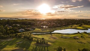An aerial view of a golf course with a lake, surrounded by residential areas and trees.