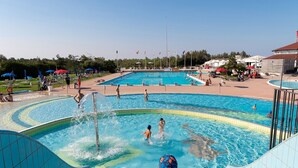 A swimming pool with multiple lanes and a water slide, surrounded by a tiled deck and umbrellas.