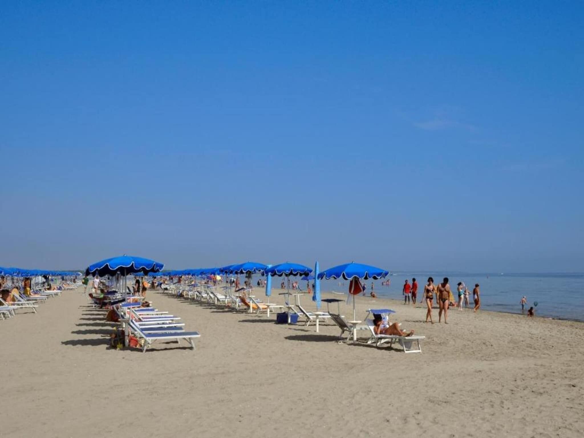 A beach with rows of sun loungers and umbrellas, a clear sky, and the ocean in the background.