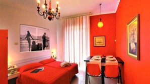 Habitación de hotel con cama, una mesa de comedor para dos personas, una araña y un cuadro en la pared.