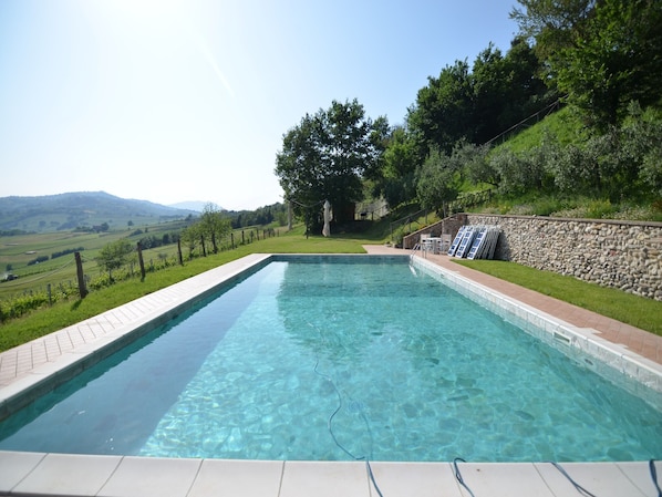 Una piscina rectangular con agua cristalina, rodeada por un muro de piedra y una zona ajardinada con vistas al campo.