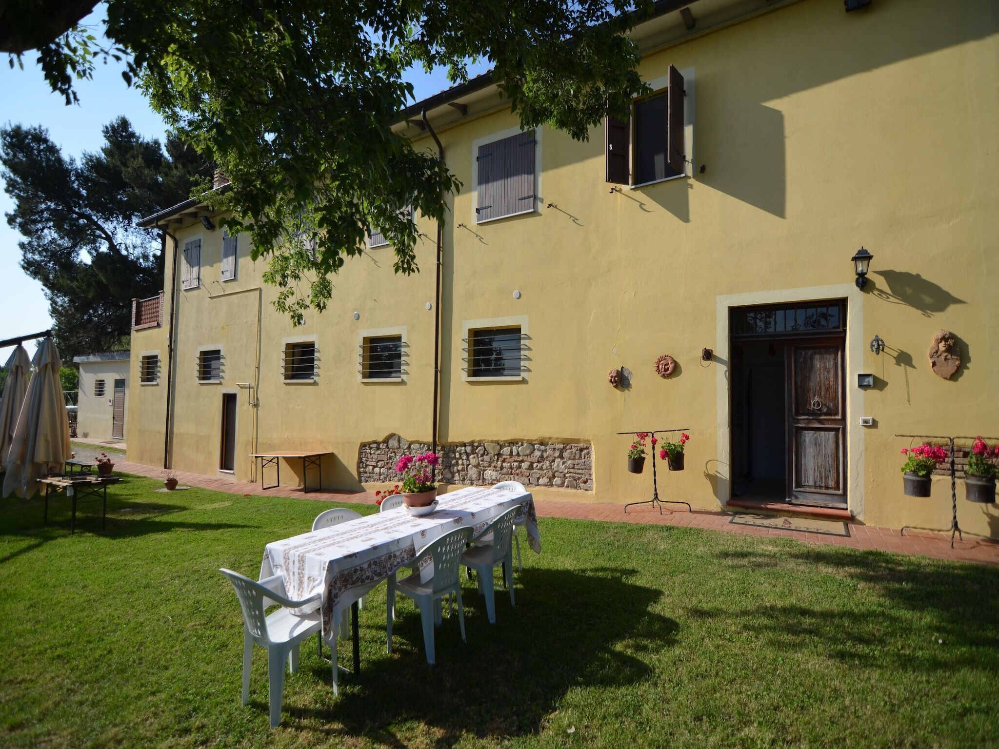 A yellow building with a stone wall entrance, a table with chairs, and potted plants.