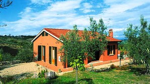 Une maison de plain-pied avec un toit recouvert de tuiles rouges, entourée de verdure et d’arbres.