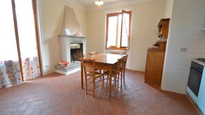 Une cuisine avec un sol carrelé, une table à manger avec des chaises, une cheminée et une fenêtre avec des rideaux.