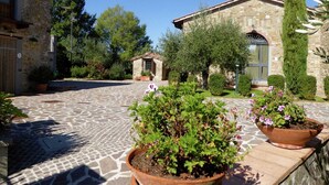 A courtyard with stone flooring, potted plants, and a stone building with a tiled roof.