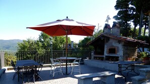An outdoor patio with a table and chairs, a red umbrella, and a stone oven.