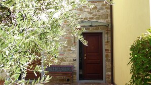 A stone building with a wooden door, a bench, and an umbrella.