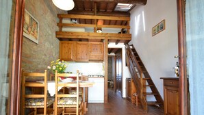 A rustic kitchen with wooden cabinets, a dining table with chairs, and a staircase leading to another level. - Montaione Oasis: Shared Villa (Montaione)