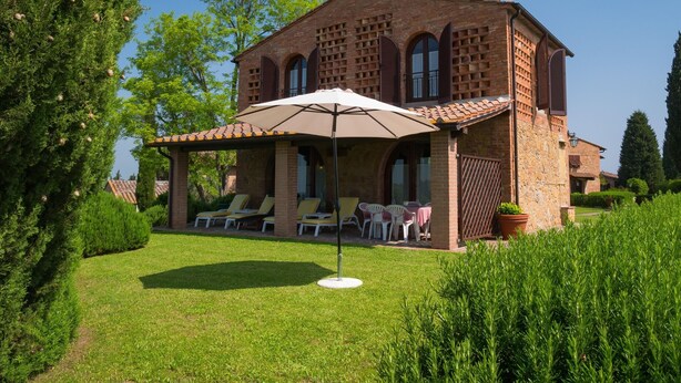 A brick house with a patio area, outdoor seating, and a large umbrella. - Montaione Oasis: Shared Villa (Montaione)